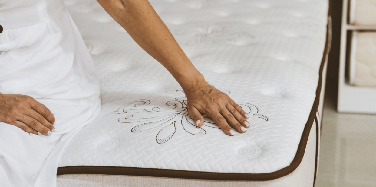 woman sitting at the edge of a mattress with her hand on the top to feel its softness  