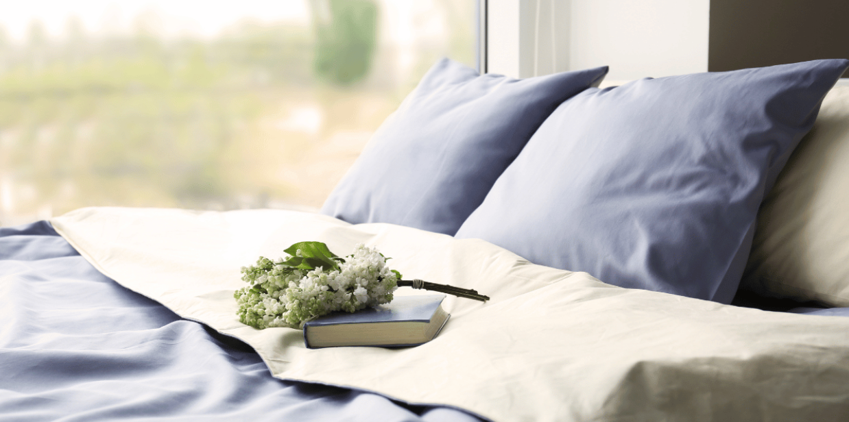 closeup of white and blue bedding on a bed with a field visible in the window in the backdrop 