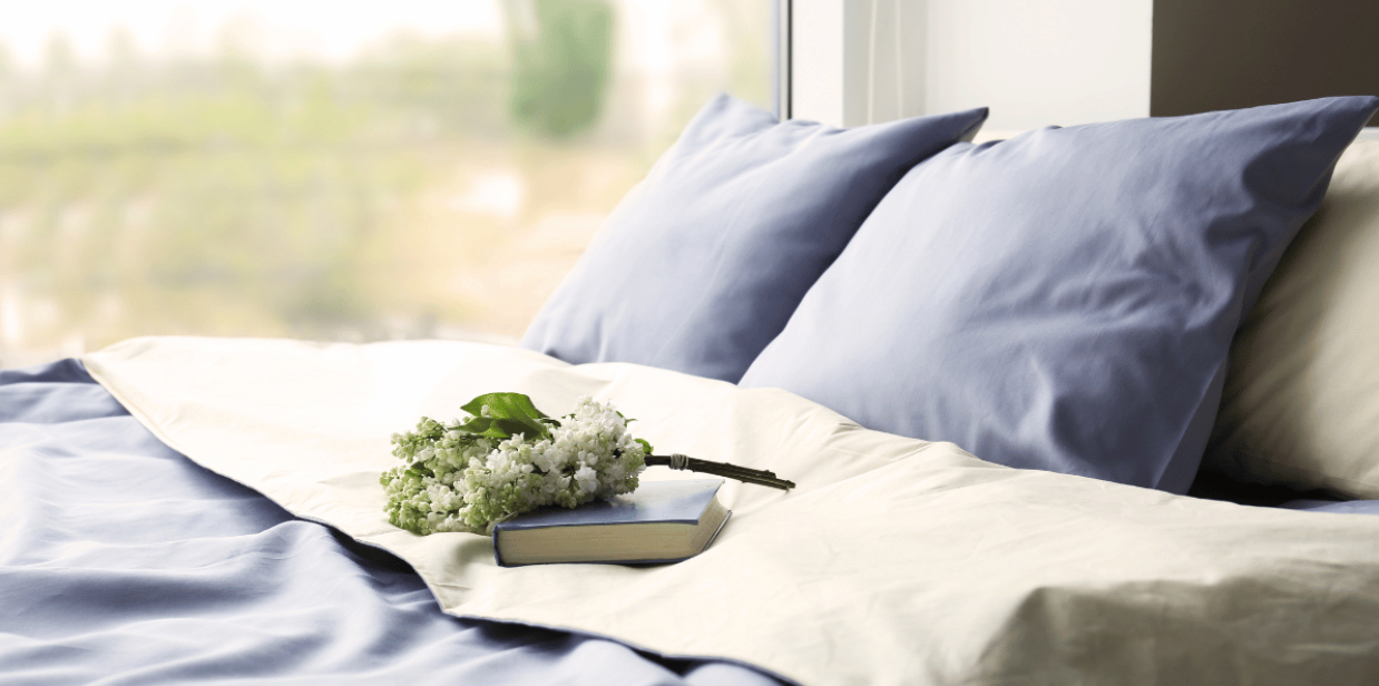 closeup of white and blue bedding on a bed with a field visible in the window in the backdrop