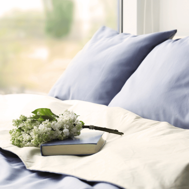 closeup of white and blue bedding on a bed with a field visible in the window in the backdrop
