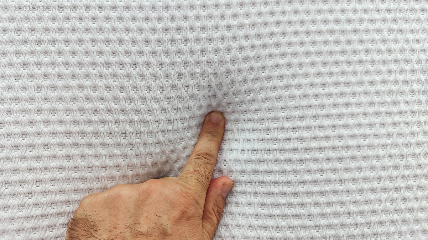 Index finger of a man’s hand pressing down on a mattress.