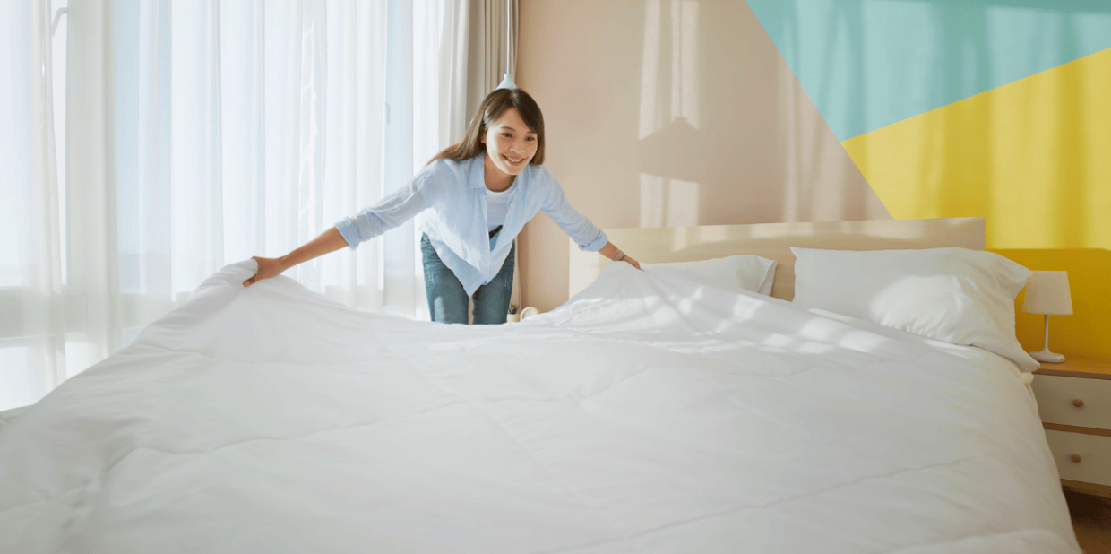 woman laying a freshly cleaned, white duvet on a bed 