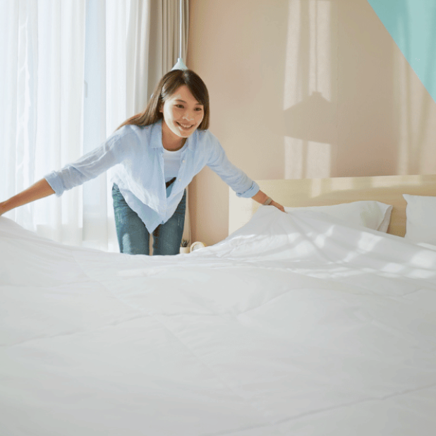 woman laying a freshly cleaned, white duvet on a bed 