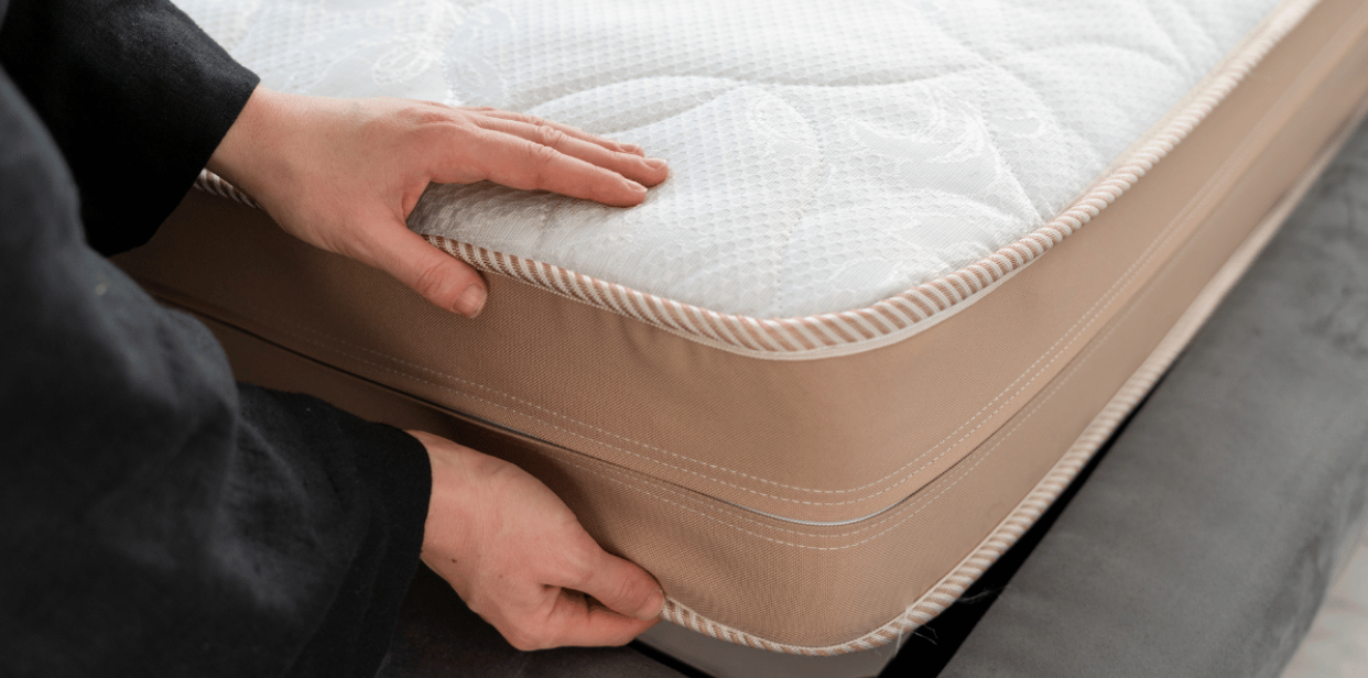 closeup of person’s hands and arms with black sleeves positioning a mattress on its base