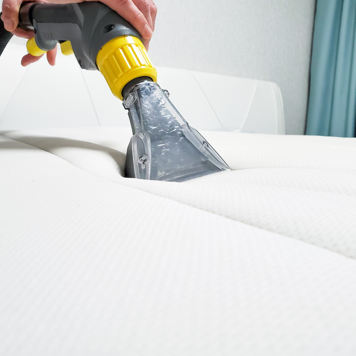 closeup of person vacuuming a mattress with an upholstery attachment
