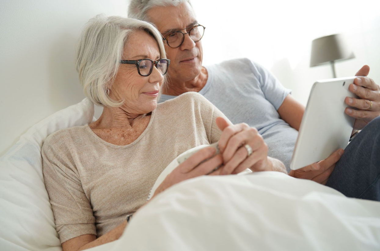 Ederly couple sitting up in bed reading from a tablet device together