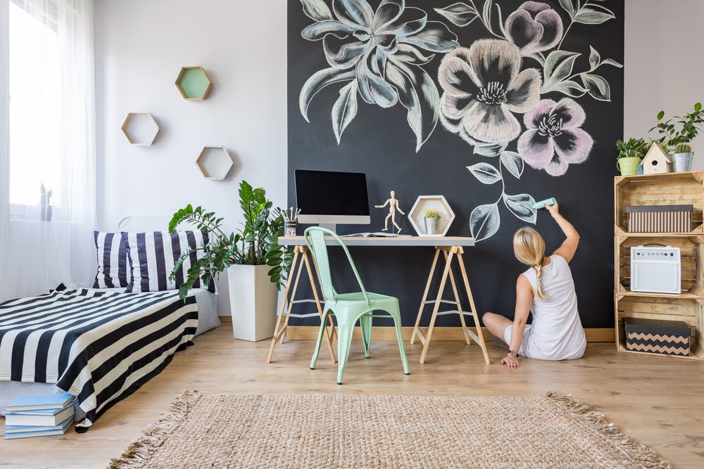 woman sitting on the floor of a bedroom drawing on a chalkboard wall