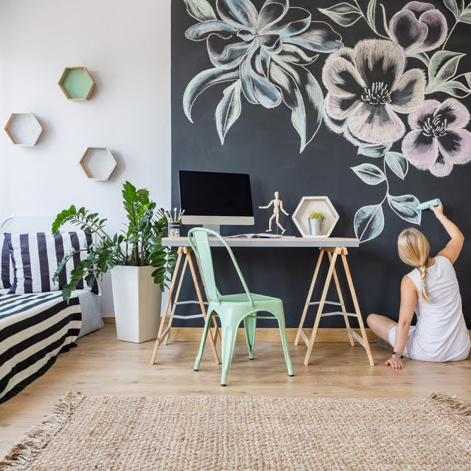 woman sitting on the floor of a bedroom drawing on a chalkboard wall