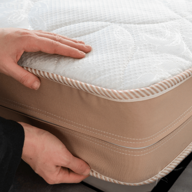 closeup of person’s hands and arms with black sleeves positioning a mattress on its base