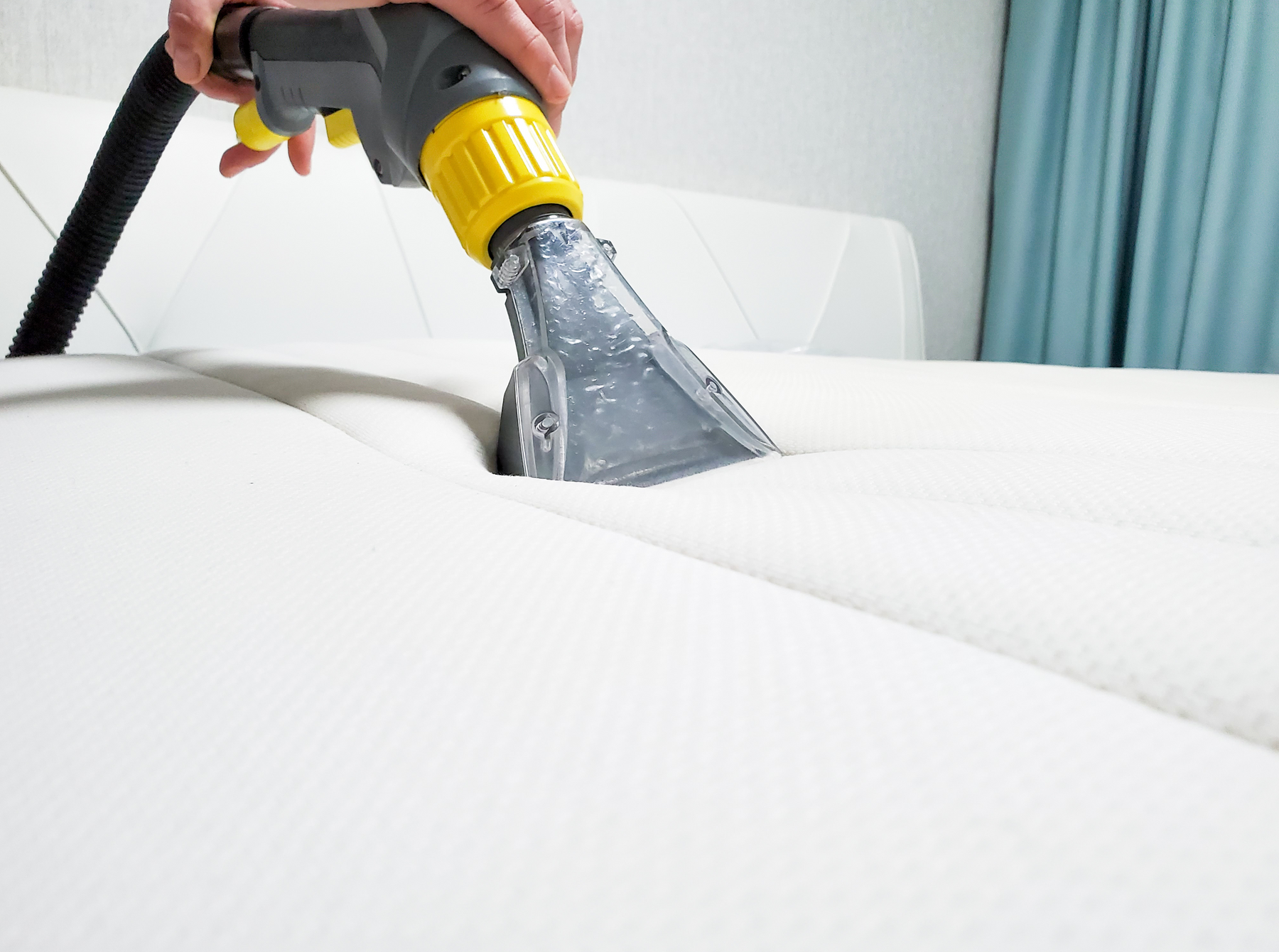 closeup of person vacuuming a mattress with an upholstery attachment