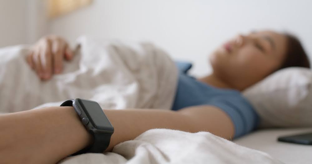 woman sleeping in bed with an Apple watch in focus in the near frame of the shot