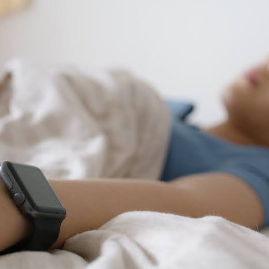 woman sleeping in bed with an Apple watch in focus in the near frame of the shot