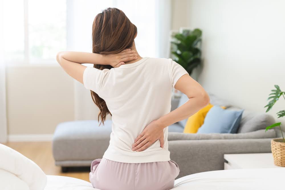 woman sitting up in bed with a sore lower back and neck